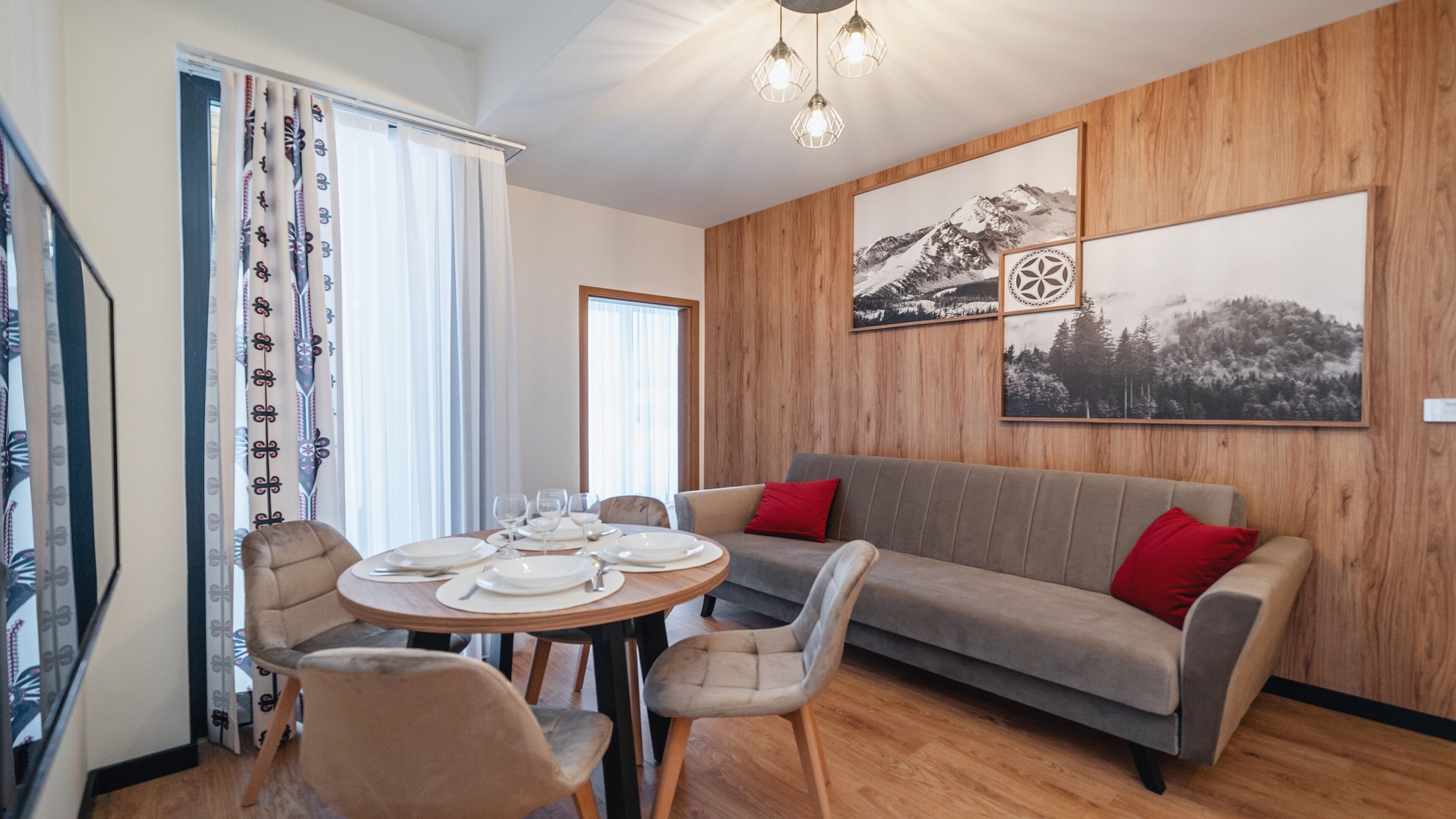 Ein Essbereich mit einem runden Tisch, gedeckt für vier Personen, einer Couch mit roten Kissen und Holzvertäfelung an den Wänden.