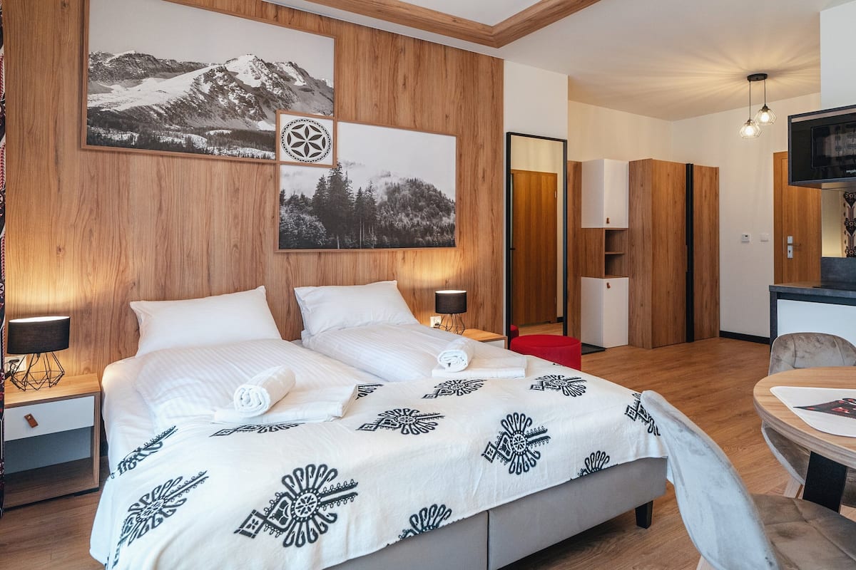 Ein Hotelzimmer mit einem großen Bett, Holzwandverkleidung, einer Essecke mit Tisch und Stühlen sowie einer Küchenzeile mit einer Mikrowelle.