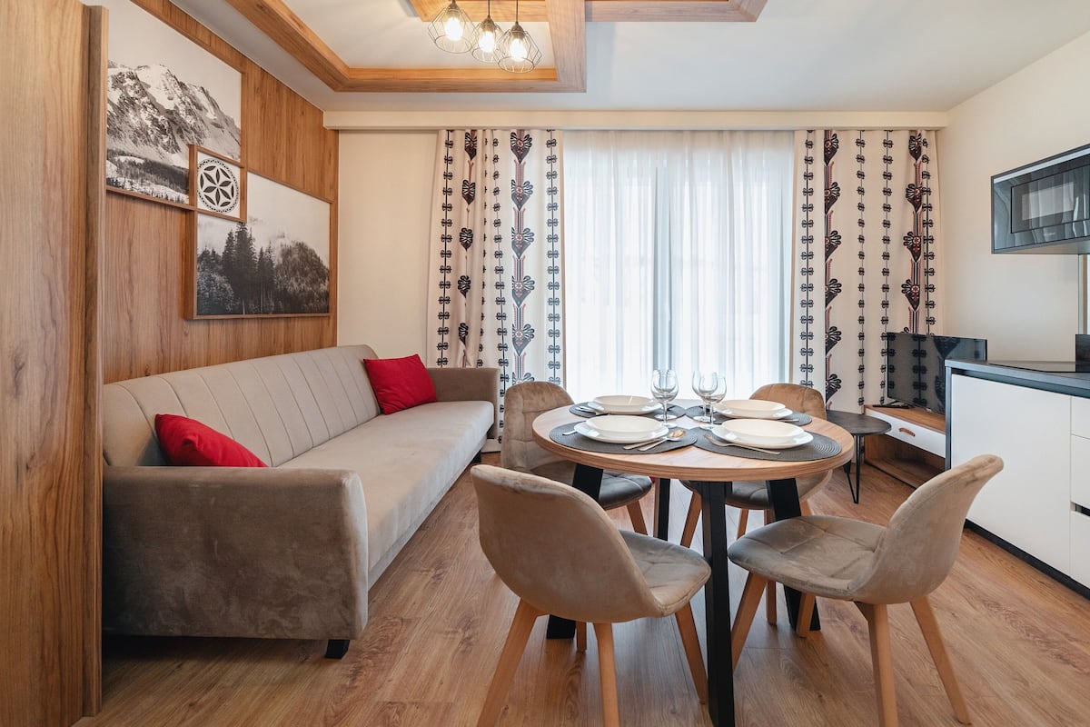 Ein gemütliches Wohnzimmer mit einer Couch, Esstisch, Stühlen und einer Küchenzeile inklusive Mikrowelle.