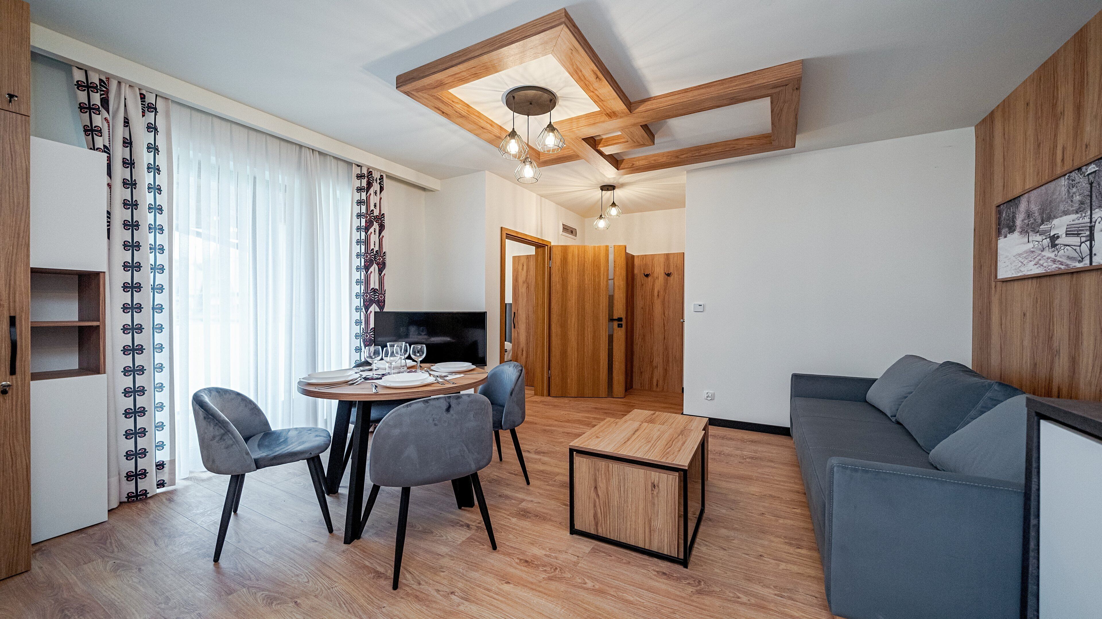 A modern living room with a dining area, wooden flooring, and a grey sofa.