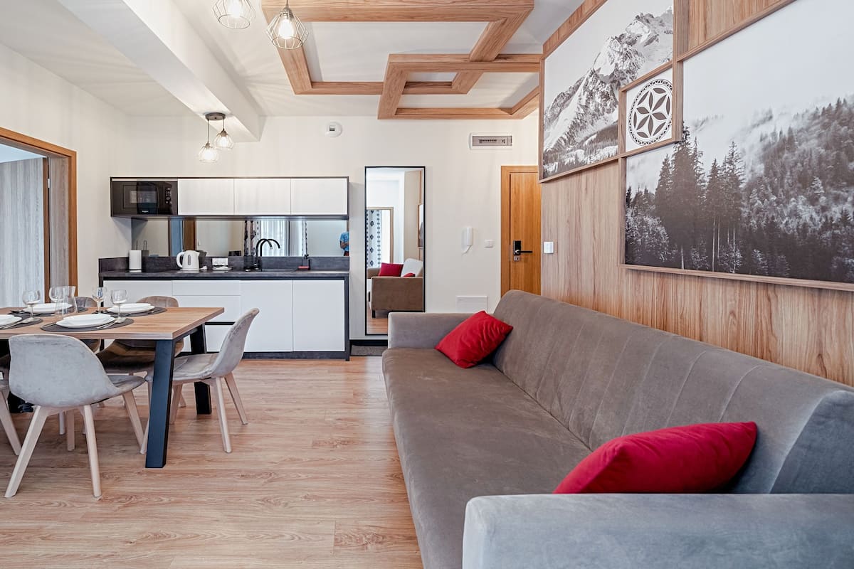 Ein moderner Wohnraum mit Essbereich, einer Küche und einem Sofa mit roten Kissen.
