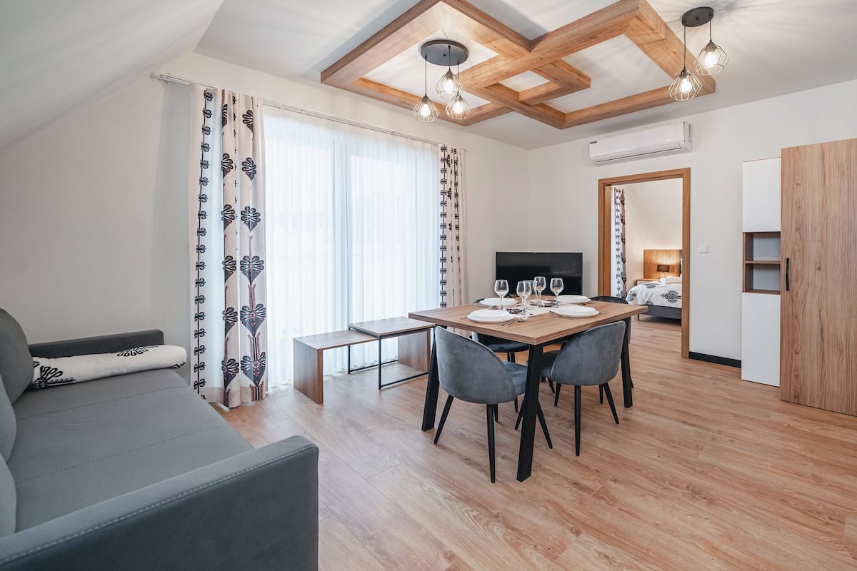Ein modernes Wohnzimmer mit einer Couch, einem Esstisch für vier Personen und einer Küchenzeile mit Arbeitsfläche und Schränken.