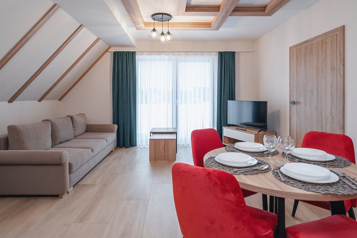 Ein modernes Wohnzimmer mit einer Couch, einem Esstisch für vier Personen und einem Fernseher.