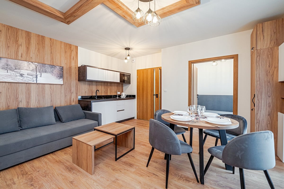 Ein modernes Wohnzimmer mit einem grauen Sofa, einem Holztisch und einem Essbereich mit rundem Tisch und Stühlen.