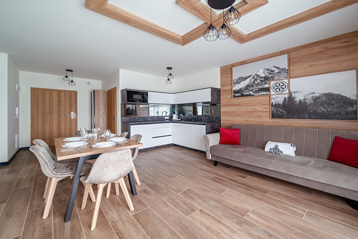 Ein modernes Wohnzimmer mit Essbereich, Holzboden und einer Couch mit roten Kissen.
