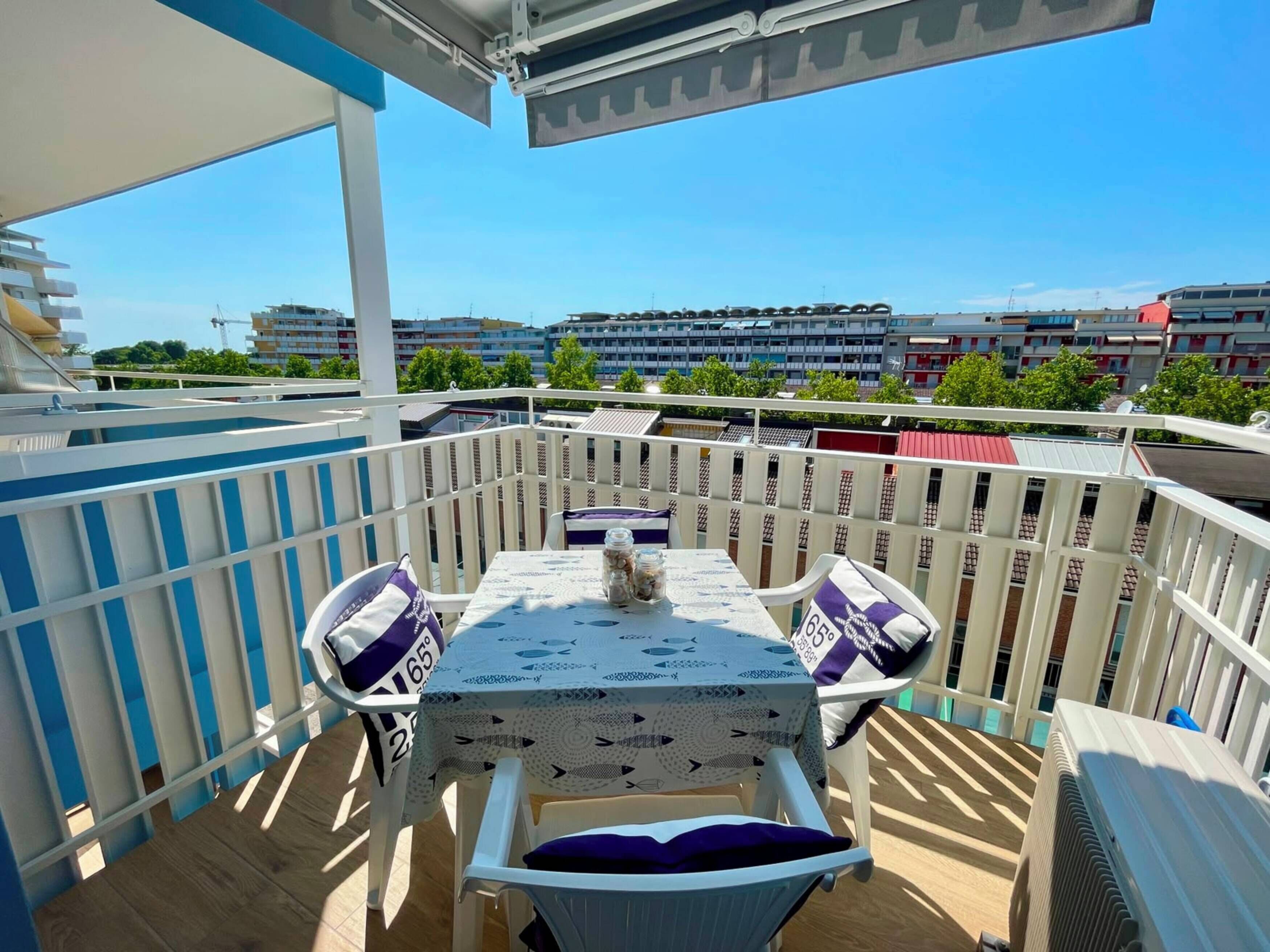 A balcony with a table and chairs, a view of buildings, and a clear sky.
