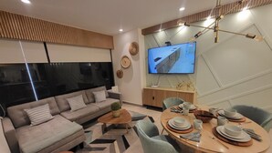 A modern living room with a sofa, coffee table, dining table set for four, and a TV mounted on the wall.