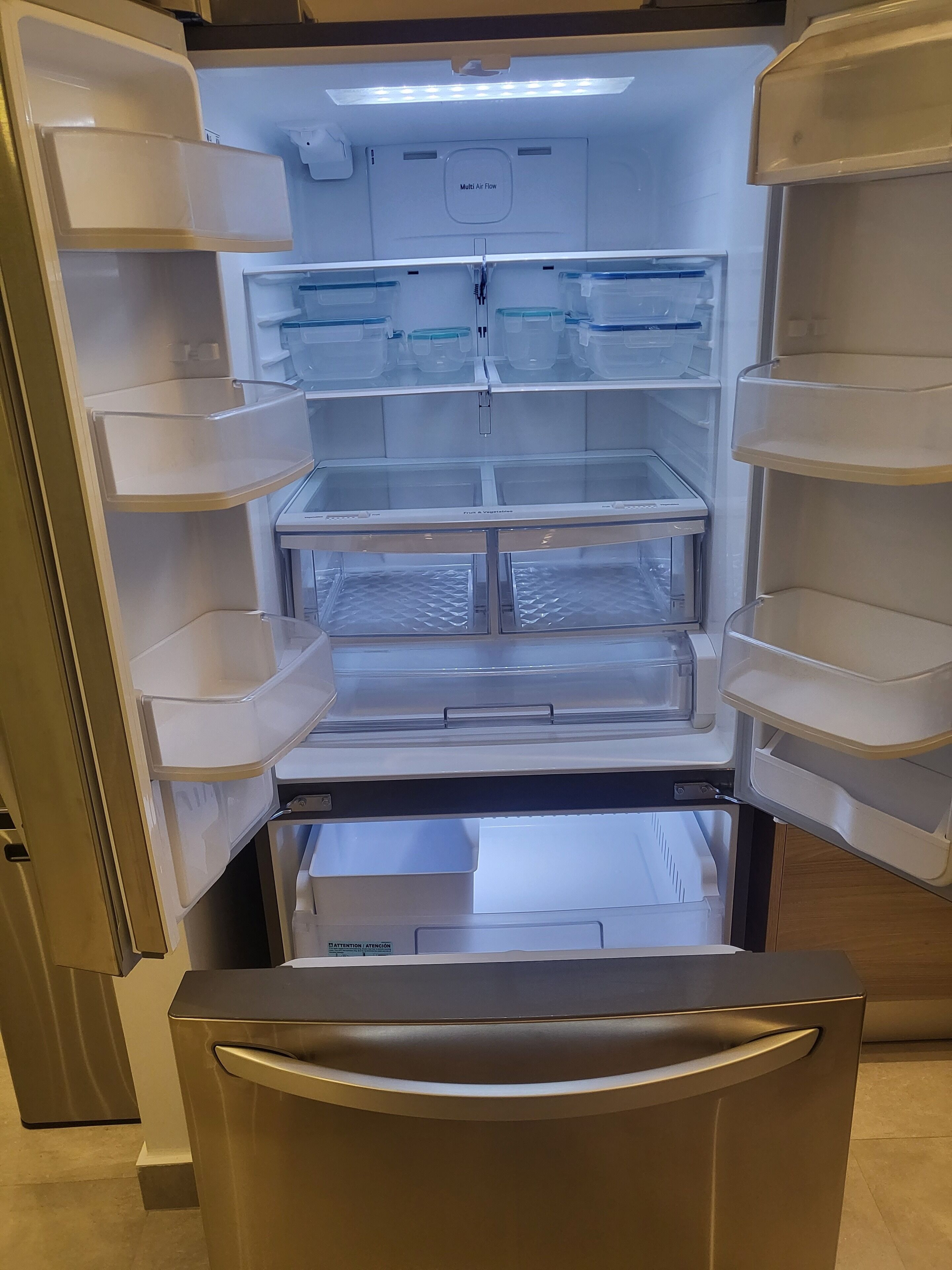 An open refrigerator with multiple shelves and compartments, including a fruit & vegetable drawer.