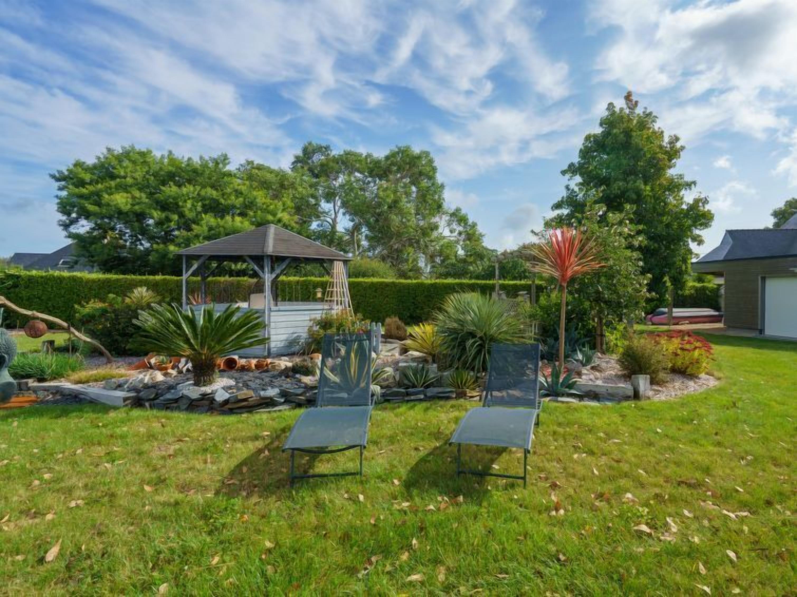 Ein Garten mit einem Gartenpavillon, zwei Liegestühlen und unterschiedlichen Pflanzen.