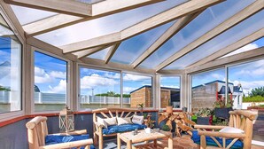 A sunroom with wooden furniture, large windows, and a view of neighboring buildings. - Guiriden by Interhome (Loctudy)
