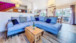 A modern living room with a blue sectional sofa, a wooden coffee table, and a staircase with a pink railing. - Guiriden by Interhome (Loctudy)