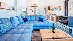 A modern living room with a blue sectional sofa, a wooden coffee table with glasses and a bottle, and a built-in fireplace. - Guiriden by Interhome (Loctudy)