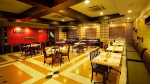 A restaurant with multiple tables and booths, a patterned floor, and a red accent wall. - HOTEL PLAZA INN (Coimbatore)