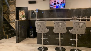 Un coin bar avec trois tabourets de bar gris, un téléviseur à écran plat fixé au mur et un comptoir en marbre.
