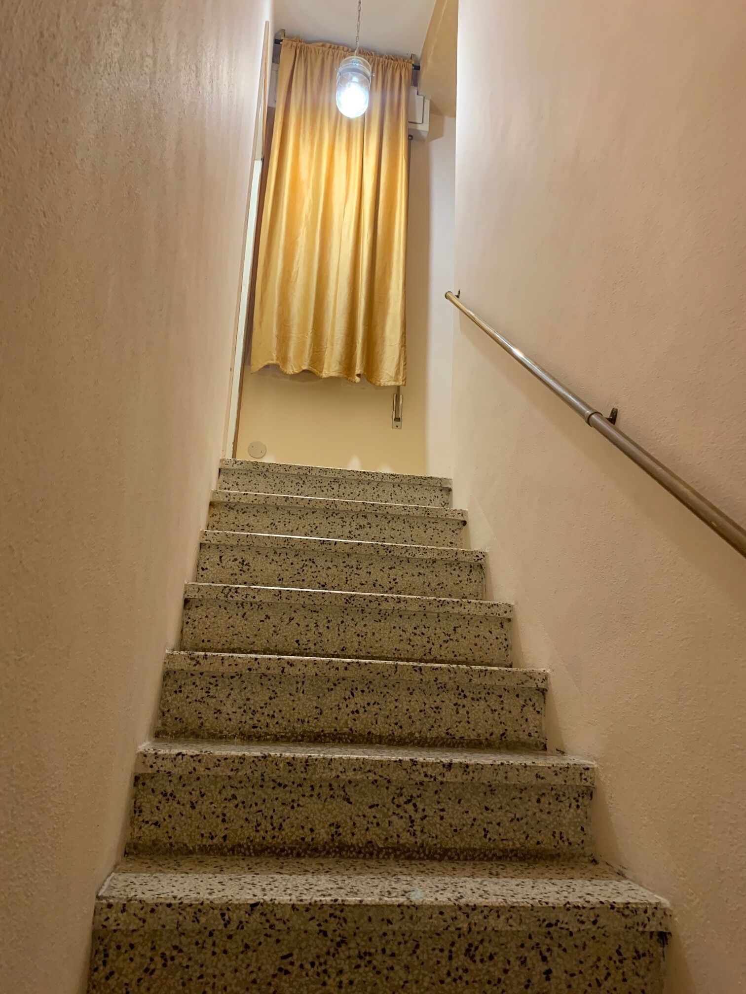 Escada com degraus salpicados levando a um quarto com luminária e cortina.