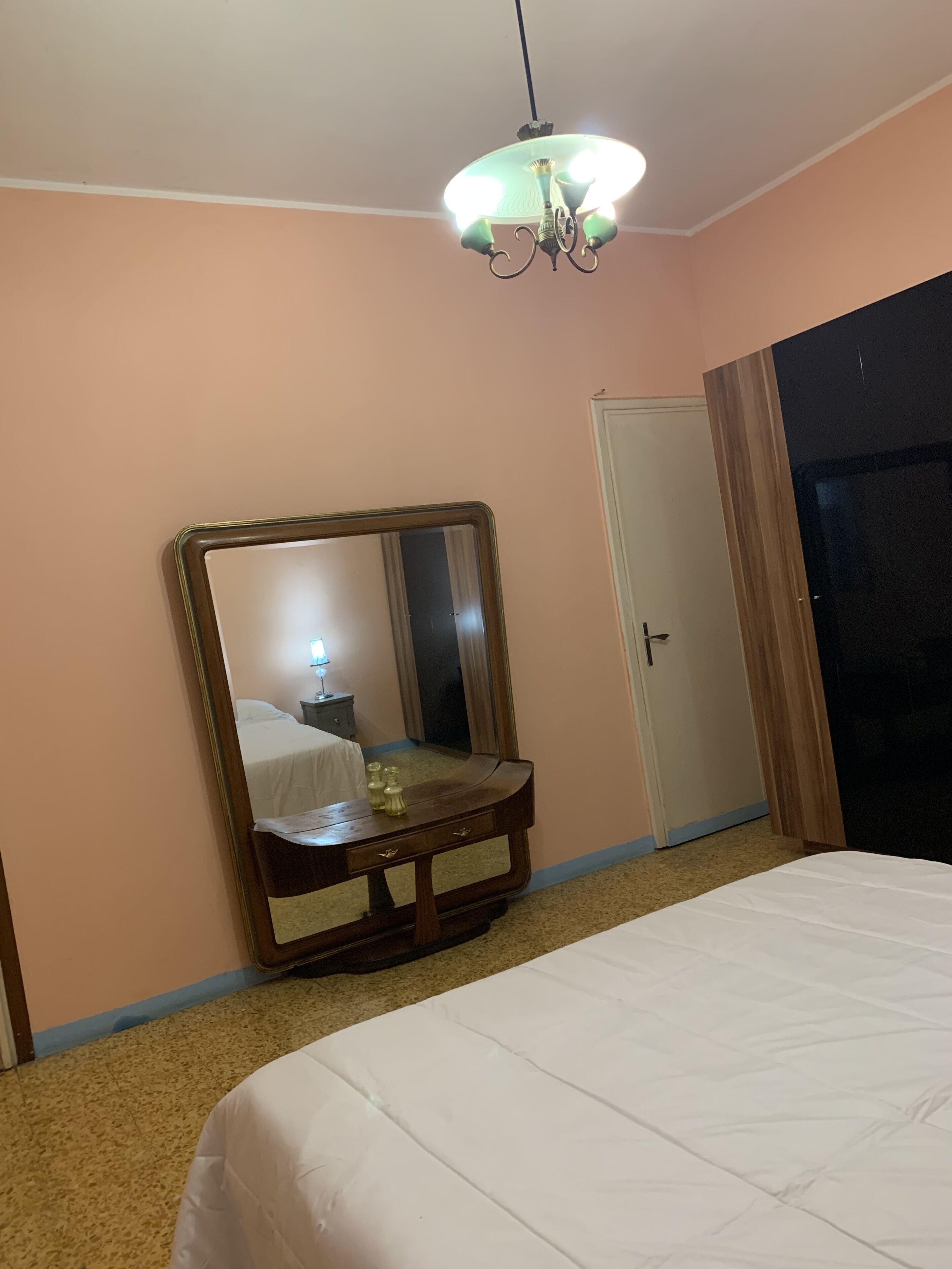 Ein Schlafzimmer mit großem Spiegel, einem Bett, einer Kommode und einer Tür.