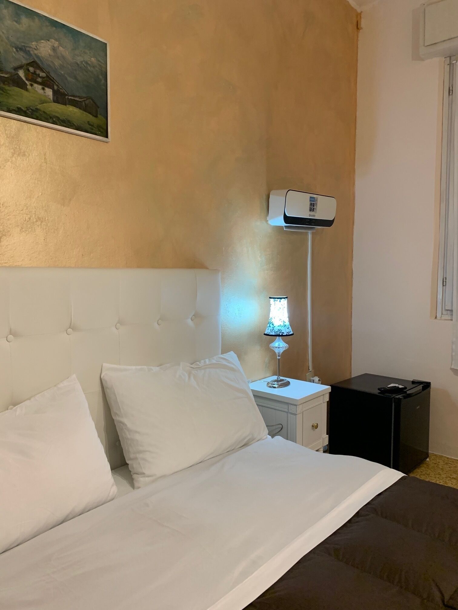 Ein Hotelzimmer mit einem Bett, einer Nachttischlampe, einem kleinen Tisch und einer Wand-Klimaanlage.