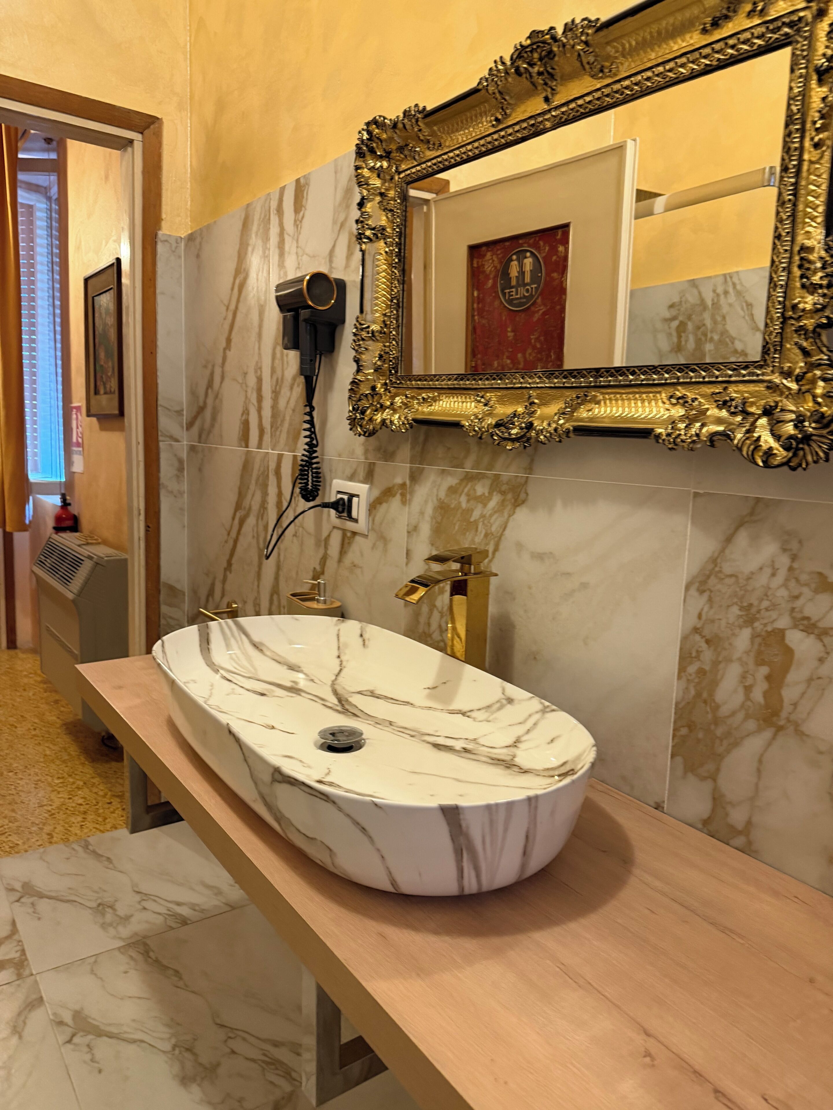A bathroom with a marble sink, gold fixtures, and a large ornate mirror.
