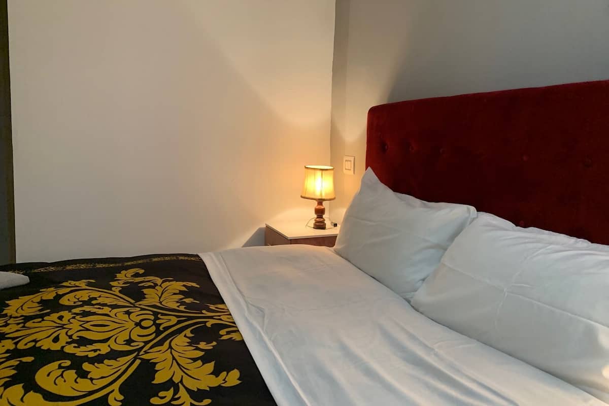 Ein ordentlich bezogenes Bett mit weißer und schwarzer Bettwäsche, einem roten Kopfteil und einer Nachttischlampe.