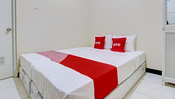 Una cama bien hecha con ropa de cama blanca y roja, una puerta blanca y un radiador blanco.