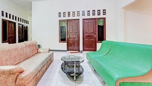 Sala de estar con un sofá, un sofá verde y una mesa de centro de vidrio. Hay dos puertas de madera y una pared con cuadros.