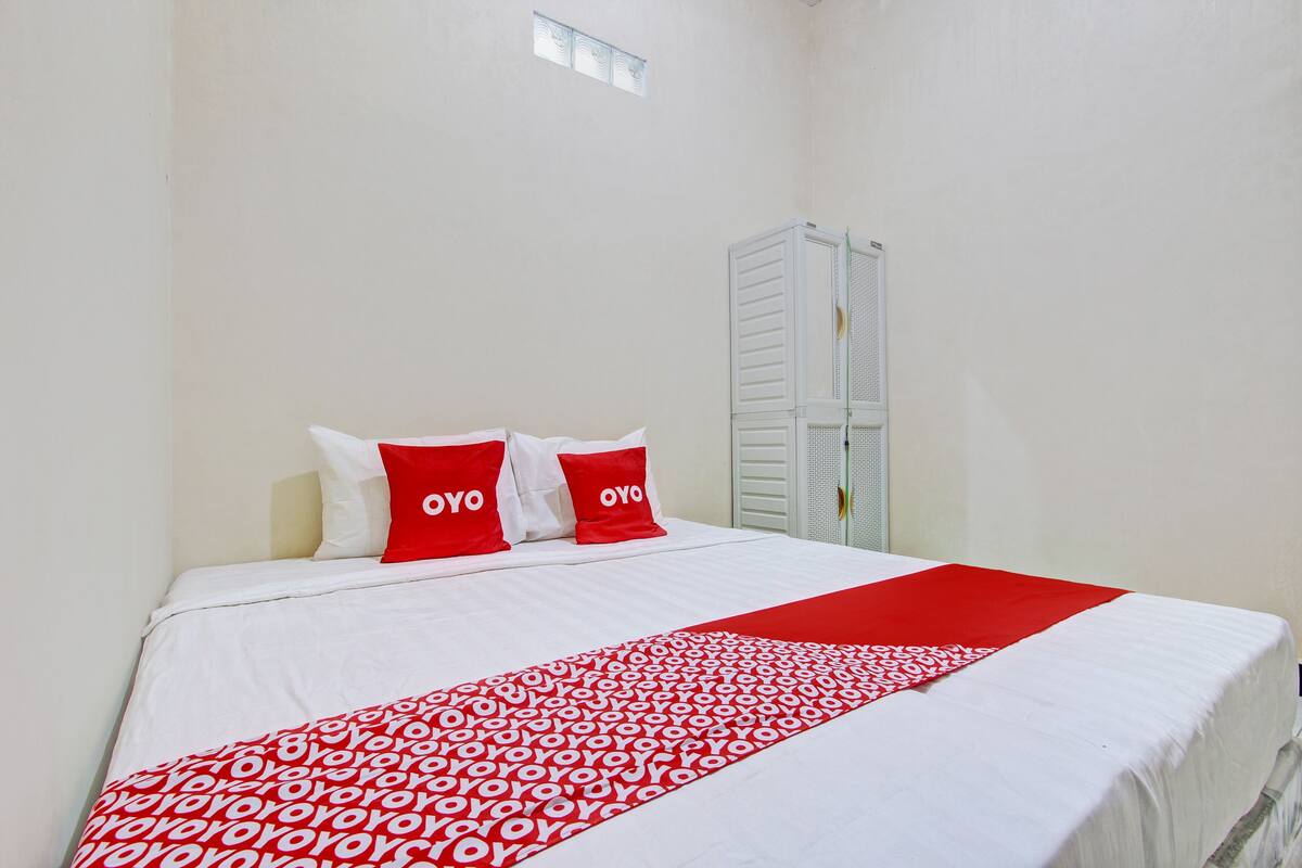 Een net opgemaakt bed met wit en rood beddengoed, inclusief kussens met de tekst "OYO" erop.