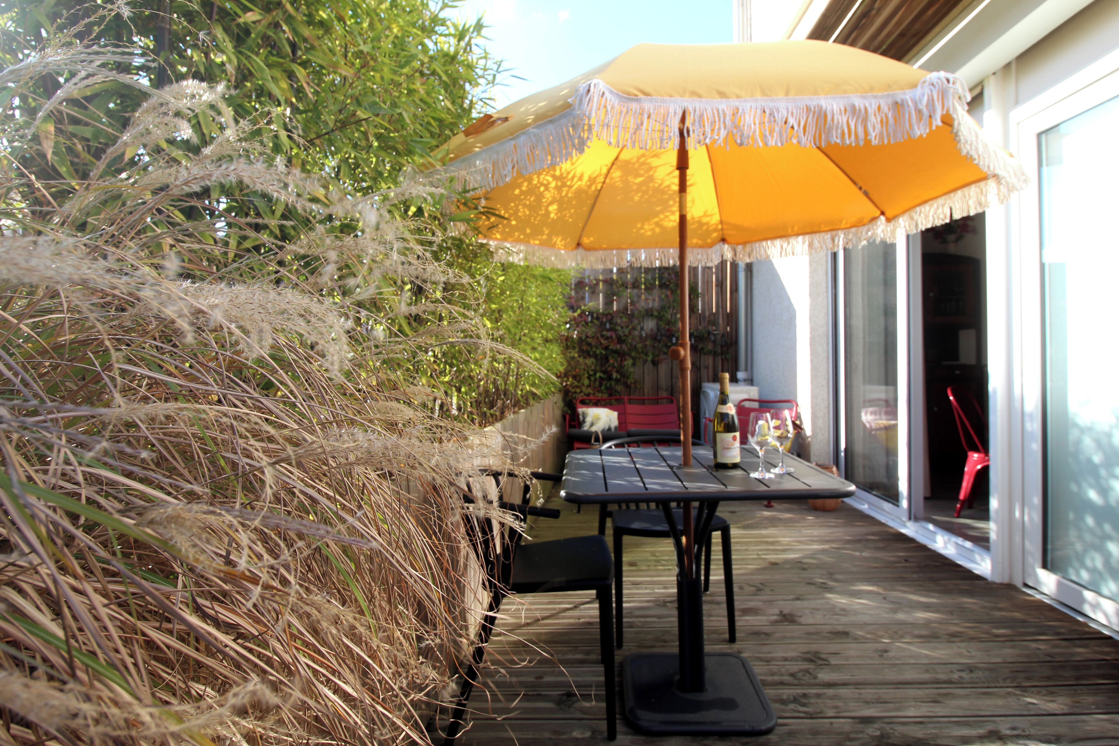 Une terrasse extérieure avec une plateforme en bois, un parasol jaune et une table entourée de chaises.