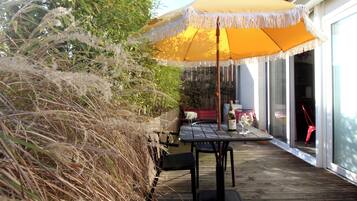Une terrasse extérieure avec une plateforme en bois, un parasol jaune et une table entourée de chaises.