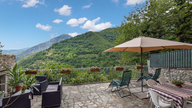 A terrace with wicker furniture, a table with a striped tablecloth, and potted plants. - Cozy home in Limano with WiFi (Limano)