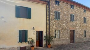 A two-story building with a stone facade and a cream-colored upper section. There are two doors with green shutters and a small potted plant in front of each door. - Cozy home in Limano with WiFi (Limano)