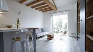Een moderne keuken met een balken plafond, een zithoek met een witte bank en barstoelen, en een groot raam met uitzicht op de omgeving.