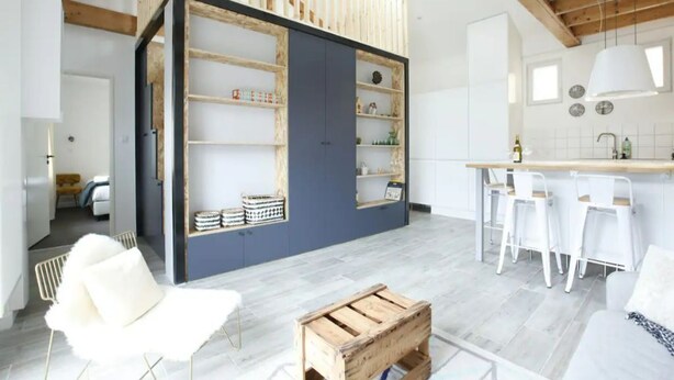 Een moderne keuken met witte barkrukken, een houten kist en een blauwe accentmuur.