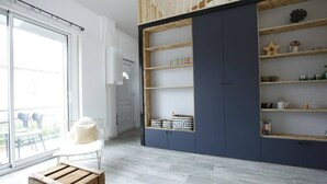 Een moderne kamer met een groot raam, een witte stoel, een houten bankje en een blauwe garderobe met planken.