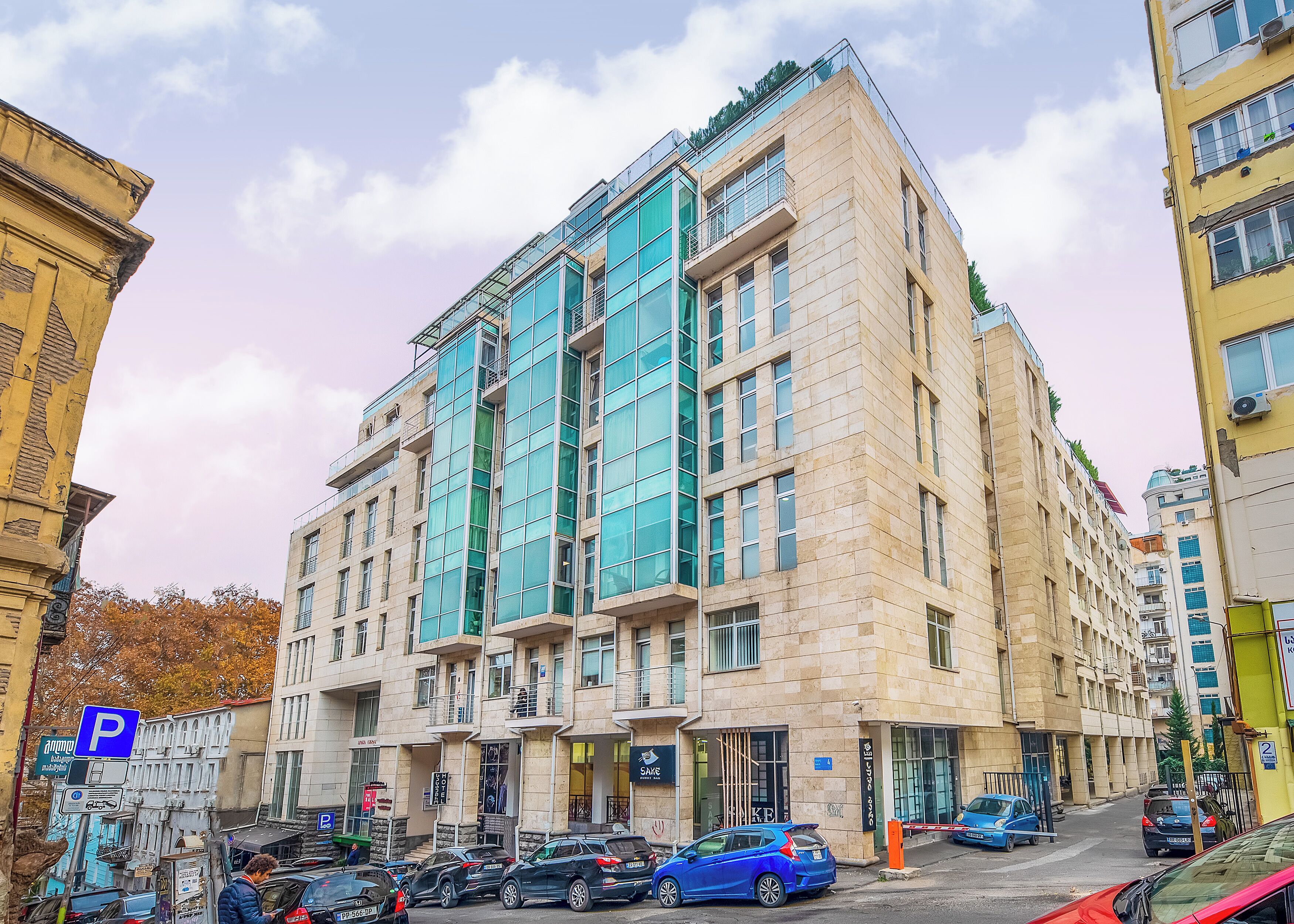 Um edifício de vários andares com fachada moderna, grandes janelas e um estacionamento em frente.
