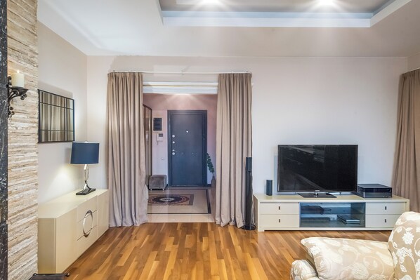 A modern living room with a flat-screen TV, a sofa, a lamp, and a wooden floor.