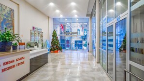 A modern business center with a reception desk, potted plants, a Christmas tree, and glass doors leading to the interior. - HB apartments Besik (Tbilisi)