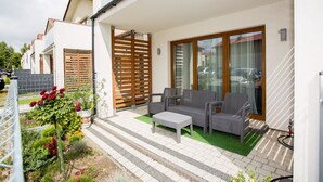 Une terrasse avec des meubles d’extérieur, une clôture en bois et un jardin fleuri.