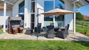 A modern house with a patio area featuring wicker furniture and a large umbrella. - Modernes Ferienhaus mit Kamin, Garten und Eigener Sauna - Ferienhaus Meerfreude (Vaschvitz)