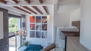 A modern living room with a blue sofa, a glass staircase, and a bed on the upper level. - Seaview Villa with pool Hanja (Podostrog)
