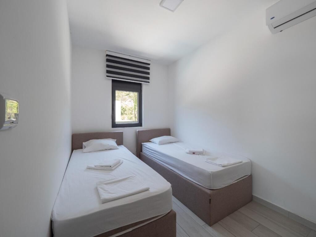 Una habitación pequeña y limpia con dos camas individuales, una ventana con persianas y aire acondicionado instalado en la pared.