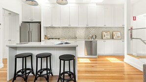 A modern kitchen with white cabinets, a stainless steel refrigerator, a built-in dishwasher, and a central island with three black stools.