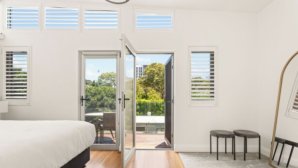 A bedroom with a bed, a sliding glass door to a balcony, and a view of greenery outside.