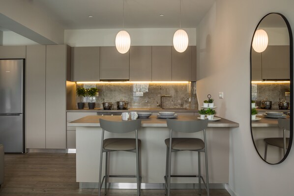 A modern kitchen with a central island, two bar stools, pendant lighting, and a large mirror.