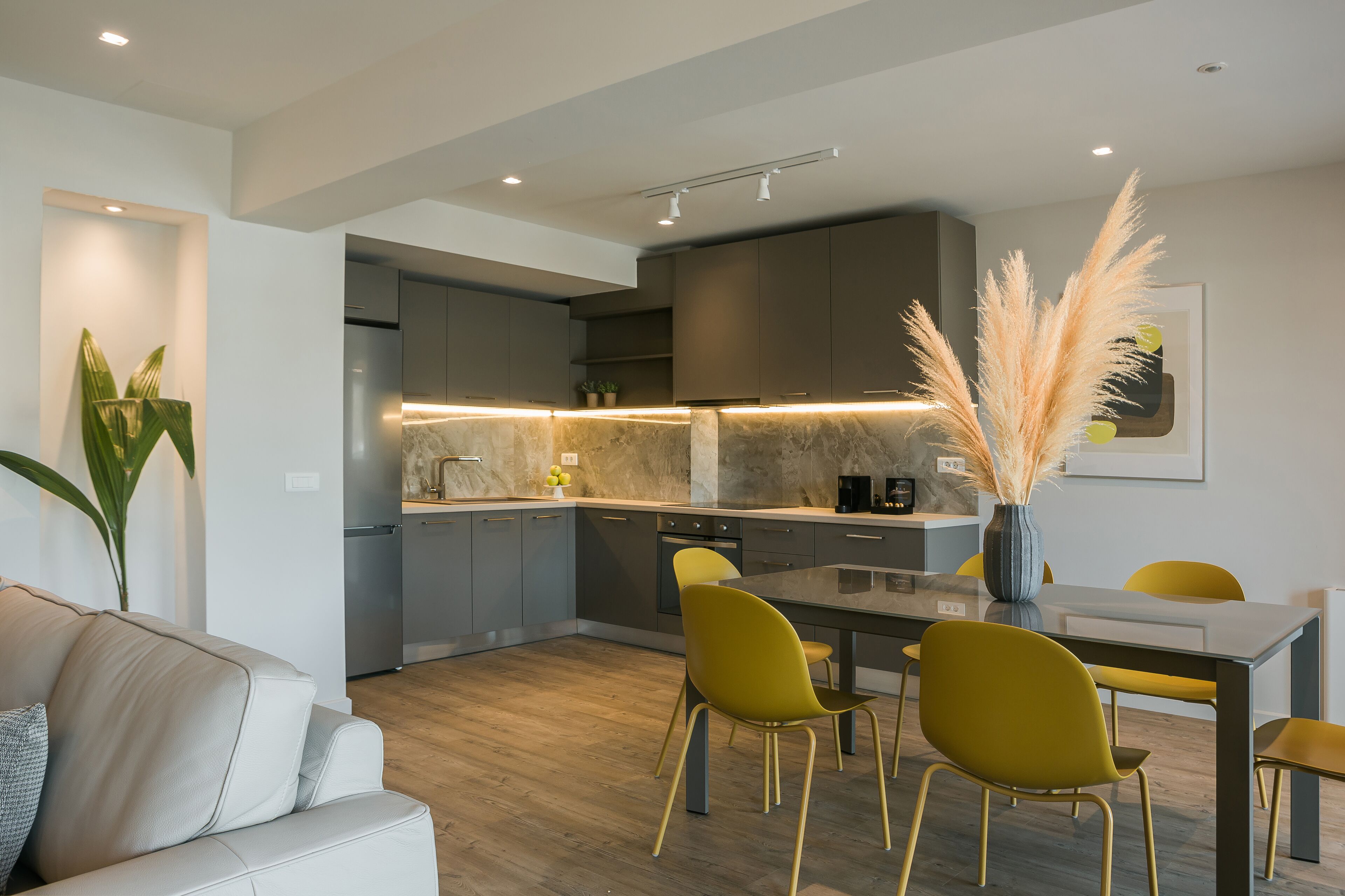 Una cocina moderna con gabinetes grises, una isla central y sillas amarillas.