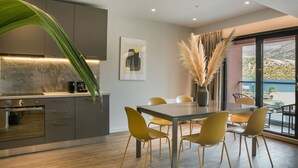 A modern kitchen with a built-in oven, a dining area with yellow chairs, and a large window offering a view of the outdoors.