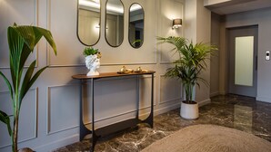 A modern hallway with a marble floor, a console table with decorative items, three wall mirrors, and potted plants.