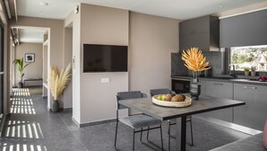 Ett modernt kök med grå skåp, en platt-TV, ett matbord med stolar och en vas med pampasgräs.