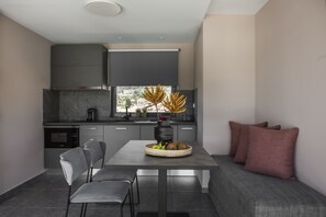 A modern kitchen with grey cabinets, a dining table with a fruit basket, and a grey sofa with cushions.