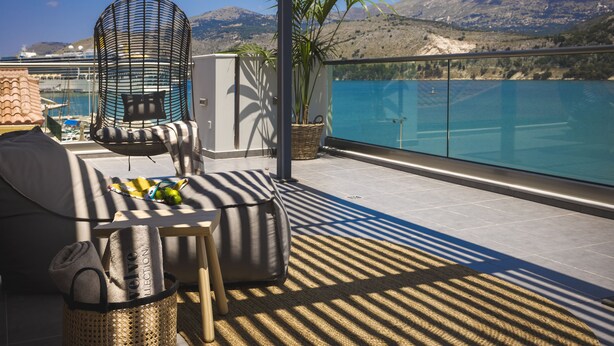 A balcony with a view of the sea, a hanging chair, a table with a basket, and a potted plant. - Grand Terrace Suite/105m² - Spacious outdoor living area (Argostoli)