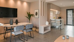 A modern dining area with a marble table, grey upholstered chairs, a large potted plant, and a flat-screen TV mounted on the wall. - Grand Terrace Suite/105m² - Spacious outdoor living area (Argostoli)